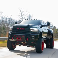 a black ram truck driving down the road with red wheels on it's tires