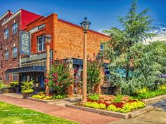 an old brick building with flowers in the front yard and trees on the other side