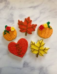 four embroidered autumn leaves and two pumpkins on a marble surface