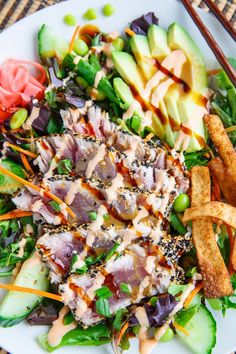 a white plate topped with salad and fries next to chopsticks on a table