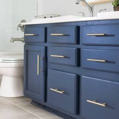 a white toilet sitting next to a blue cabinet in a bathroom under a mirror with gold handles