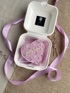 a pink heart shaped cake in a white box with a purple ribbon on the side