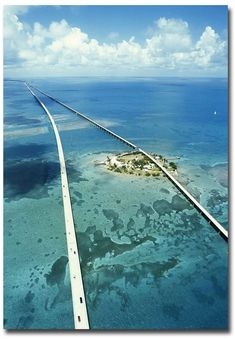 an island in the middle of water with a road going through it and blue skies above