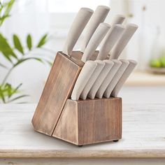 a wooden block holding many knives on top of a white table next to a potted plant