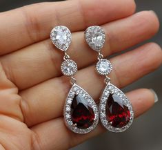 a pair of red and white diamond earrings in someone's hand with their fingers