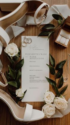 wedding stationery with white roses, rings and shoes on a table next to the bride's bouquet