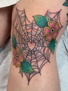 a spider web tattoo with flowers and leaves on the side of a woman's thigh