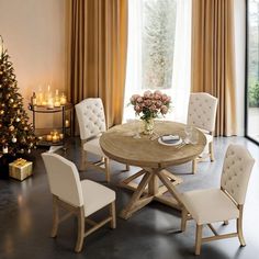 a dining room table surrounded by chairs and a christmas tree in the corner with candles on it