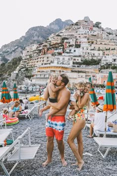 a man and woman hug each other on the beach in front of some umbrellas