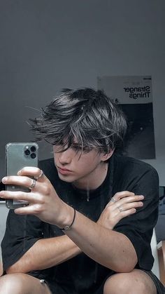 a young man sitting on the floor holding a cell phone in his hand and looking at it