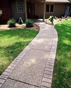 a walkway in front of a house with grass and bushes on the side of it