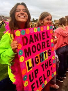 two girls holding up a sign that says daniel moore lights up the field