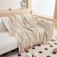 a white couch covered in a blanket next to a vase and potted plant on the floor