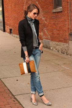 a woman is standing on the sidewalk with her handbag in her pocket and wearing jeans