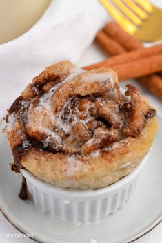 a cinnamon roll sitting on top of a white plate next to some cinnamon sticks and a fork