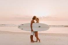 two women are standing on the beach with a surfboard in their hands and kissing