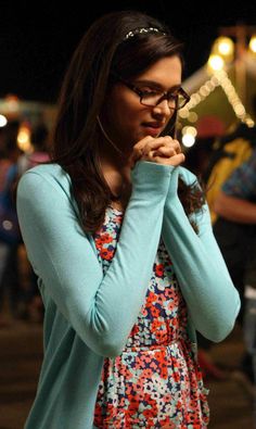 a woman standing in front of a crowd looking at her cell phone while wearing glasses