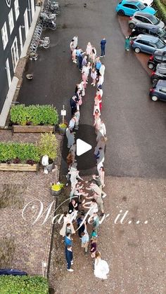 a group of people standing on top of a parking lot next to a street filled with parked cars