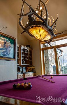 a pool table with a light fixture hanging from it's center and antlers on the ceiling