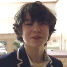 a young man with short hair wearing a blue jacket and yellow shirt is staring at the camera