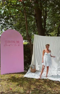 a woman standing in front of a pink sign and white cloth draped over her shoulders