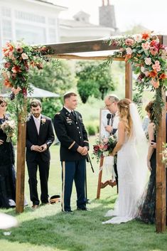 a bride and groom standing under an arch at their outdoor wedding ceremony in the grass