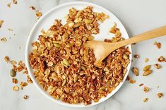 a white bowl filled with granola on top of a counter next to a wooden spoon