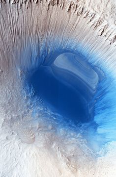 an aerial view of a blue hole in the ground with sand and water around it