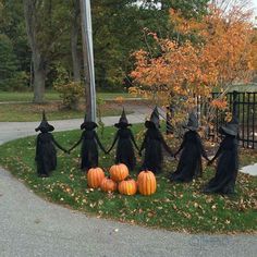 halloween decorations in the shape of witches holding hands and pumpkins on grass near fence