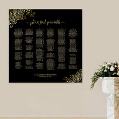 a black and gold wedding seating chart on a wall next to a vase with flowers