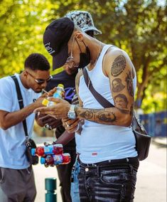 two men standing next to each other while looking at their cell phones with tattoos on them