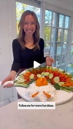 a woman standing in front of a platter filled with veggies