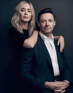 a man and woman are posing for a photo in front of a black background, one is holding the other's arm around his neck