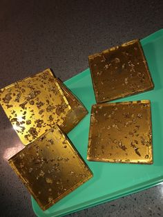 four square pieces of gold sitting on top of a green tray next to each other