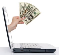 a person holding money in front of a laptop