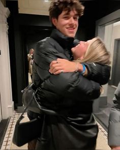 a man and woman hug in front of a fireplace