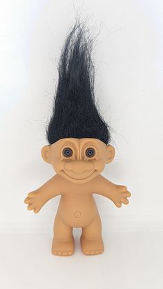 a troll doll with long black hair on it's head and eyes, standing in front of a white background