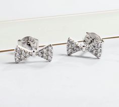 Tiny bow stud earrings that you can offer as a gift to your bridesmaids or as a treat to yourself. The stones are sparkling cubic zirconia stones. Add a playful touch to your look by adorning your ears with these chic and contemporary tiny bow stud earrings. They can be worn on multiple piercings, and they complete any outfit. They are small for that ideal and realistic look. Uses standard push back posts.- Stone Material: Cubic Zirconia.- Shape of Stones: Round Pave.- Metal: 925 Sterling Silver Formal Bow Earrings With Cubic Zirconia, Formal Bow Earrings In Cubic Zirconia, Bow Cubic Zirconia Earrings For Party, Party Earrings With Bow And Cubic Zirconia, Sterling Silver Bow Earrings For Wedding, Glamorous Diamond White Diamond Earrings As Gift, Glamorous Sterling Silver Diamond Earrings As Gift, Glamorous Sterling Silver Diamond Earrings For Gift, Bridesmaid Thank You