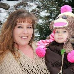 a woman is holding a child wearing a monkey hat and jacket with pink pom poms