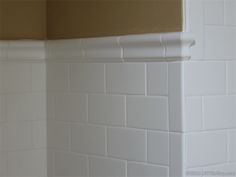 an empty bathroom with white tile walls and brown trim on the shower head, toilet paper dispenser next to it