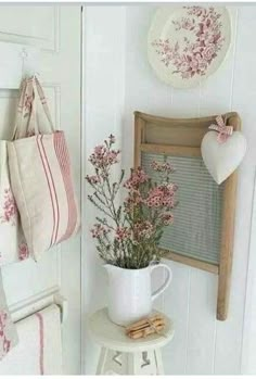 a white vase with pink flowers in it sitting on a table next to a towel rack