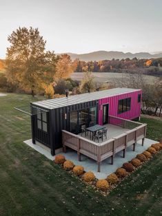 a house made out of shipping containers in the middle of a field with trees and grass around it