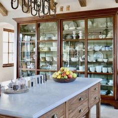 a large kitchen island topped with lots of counter space and glass front cabinets filled with dishes