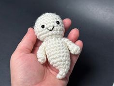 a hand holding a small white crocheted stuffed animal