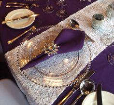 the table is set with silverware and purple napkins, along with other place settings