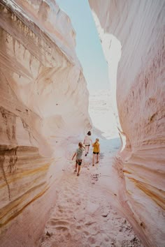 three people are walking in the sand between two cliffs