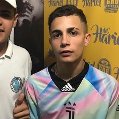 two young men standing next to each other in front of a yellow wall with a poster behind them