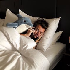 a man laying in bed with a stuffed animal on his pillow and talking on the phone