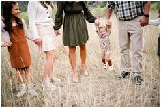 a group of people holding hands and walking through tall grass with one child in the middle