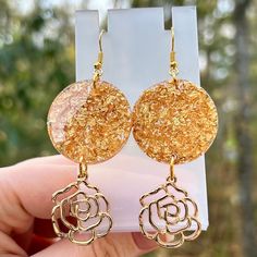 Expertly handcrafted with gold flake resin, these stunning earrings showcase delicate rose charm dangles, adding a touch of elegance to any outfit. Each pair is unique, making them a special addition to your collection. Elevate your style with these beautiful, one-of-a-kind handmade earrings. Nickle Free  Each pair of earrings is unique and handmade. Gold Dangle Earrings With Rose Design, Gold Drop Earrings With Rose Design, Gold Dangle Flower Earrings With Rose Design, Gold Flower Resin Earrings, Rose Gold Pressed Flower Earrings, Gold Dangle Resin Flower Earrings, Gold Resin Flower Charm Earrings, Cheap Flower-shaped Resin Earrings, Gold Flakes